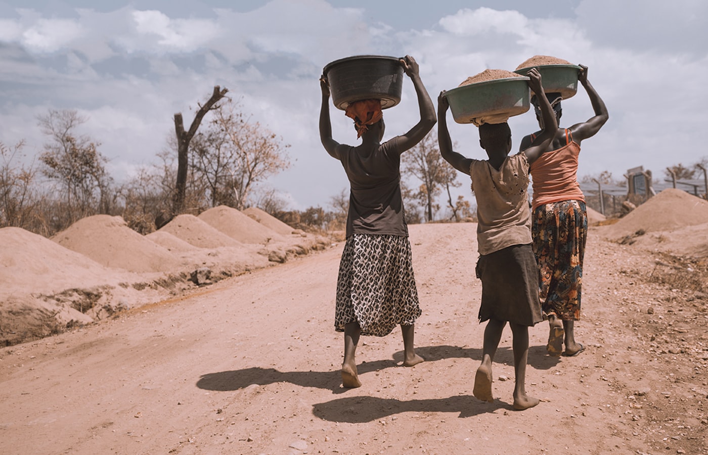 Women carrying basins of water along a dusty road